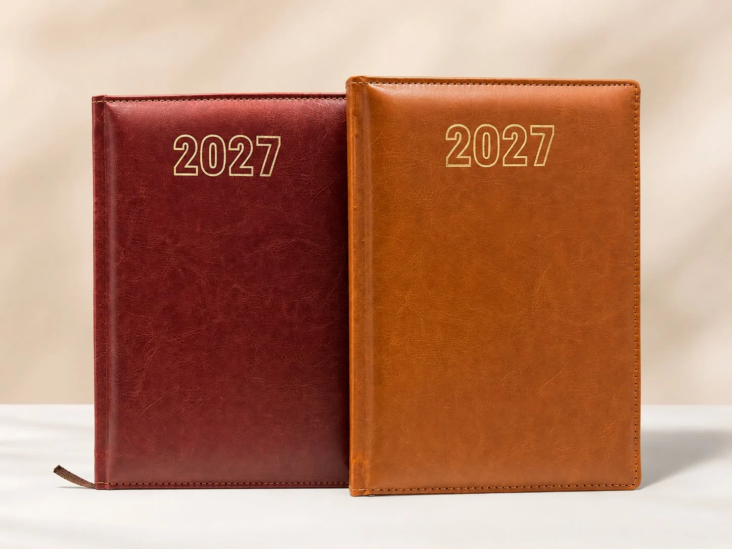 Two leather 2027 diaries in burgundy and tan with gold foil lettering